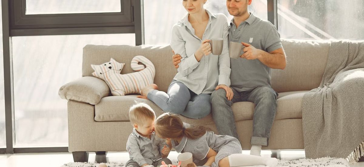 Cheerful family smiling while spending weekend together sitting parents sitting on comfortable sofa while children resting on carpet and playing