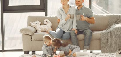 Cheerful family smiling while spending weekend together sitting parents sitting on comfortable sofa while children resting on carpet and playing