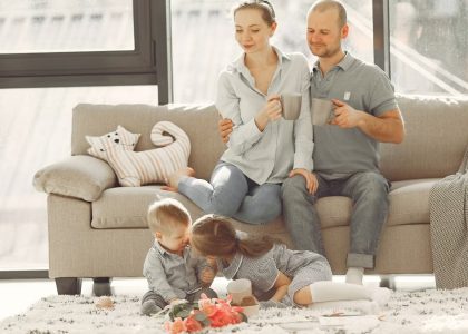 Cheerful family smiling while spending weekend together sitting parents sitting on comfortable sofa while children resting on carpet and playing