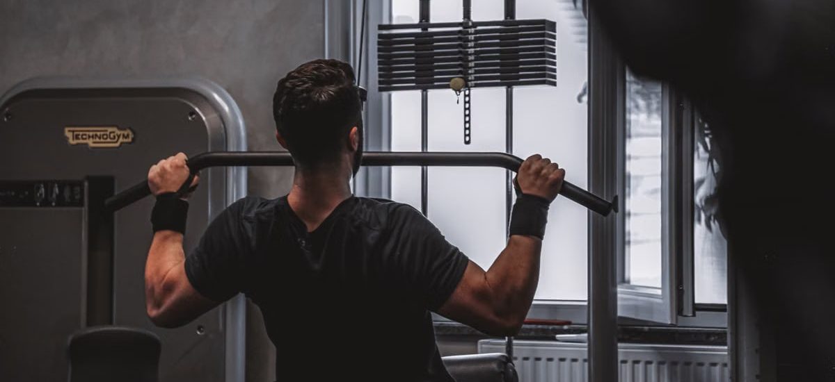 Back view of a man exercising with lat pulldown machine in the gym.