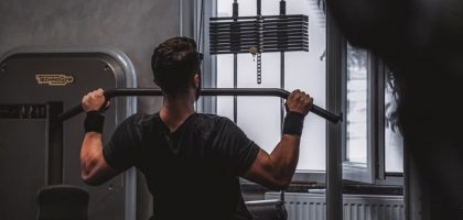 Back view of a man exercising with lat pulldown machine in the gym.